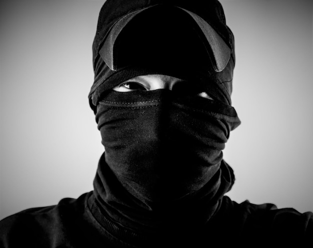 Crimineel met bivakmutsmasker Een crimineel in zwarte kleding met een bedekt gezicht