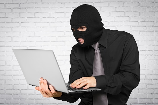 Criminele hacker die balaklava draagt met laptop op bakstenen muurachtergrond