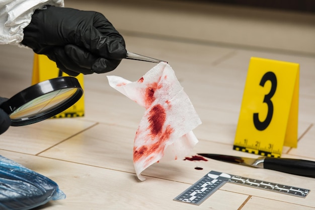 Photo a criminology expert looks through a magnifying glass at a bloody napkin at the crime scene