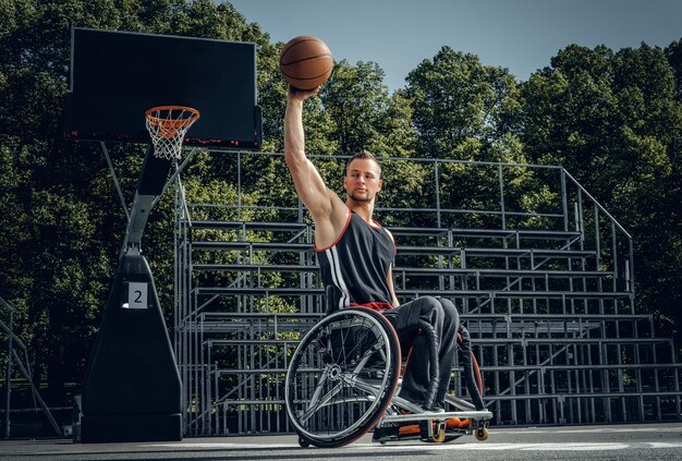 Photo cripple basketball player in wheelchair plays basketball on open air ground.