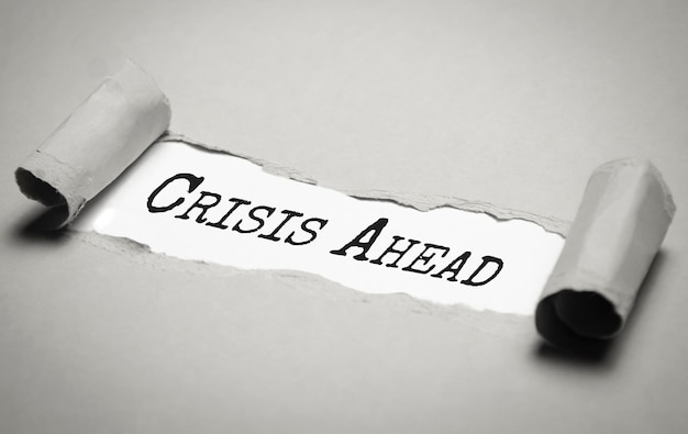 Crisis ahead think positive words text on grey paper on torn\
paper background