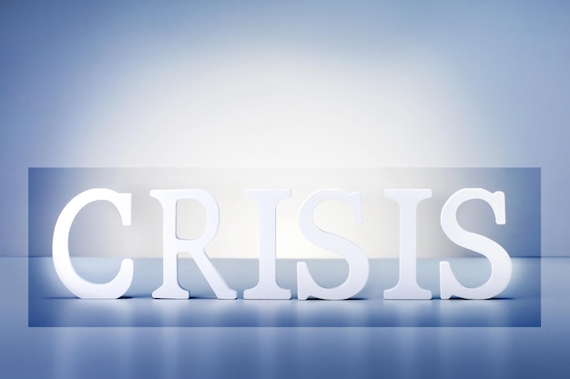 Crisis word made of wooden letters on blue grey background.