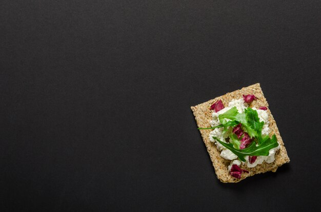 Crisp bread with soft cream cheese and herbs on black background. Top view.