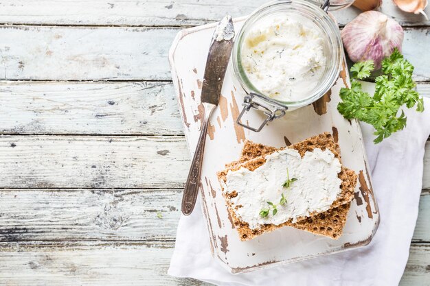 Crispbread toast with homemade herb and garlic cottage cheese on wooden background, top view