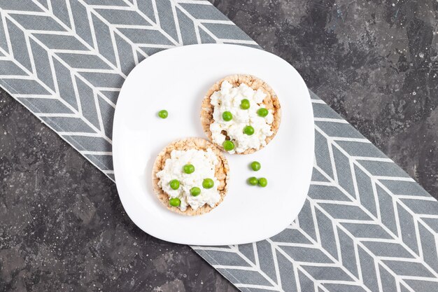 Crispbreads with cottage cheese and green peas on a white plate