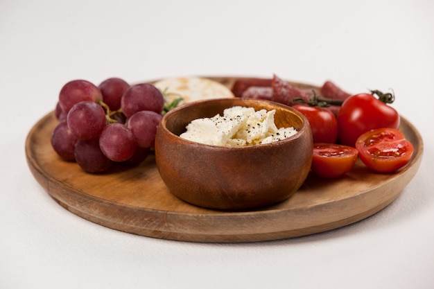 Crispy biscuits, cherry tomatoes, grapes and bowl of cheese on wooden board