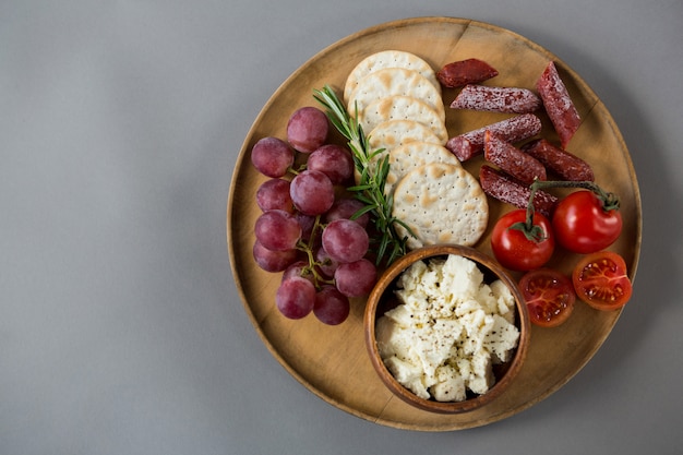 Crispy biscuits, cherry tomatoes, grapes and bowl of cheese on wooden board