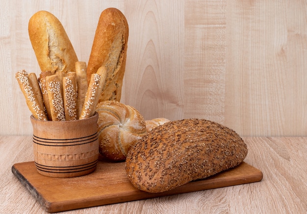 Crispy bread sticks with sesame seeds and bran bread on a wooden board. French baguettes. Different breeds on wooden background.