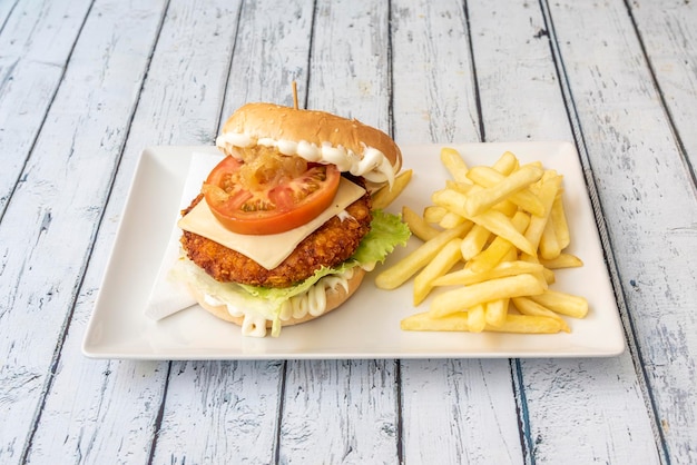 Crispy chicken burger in batter with tomato slice caramelized onion sliced cheese butt mayonnaise and a side of French fries