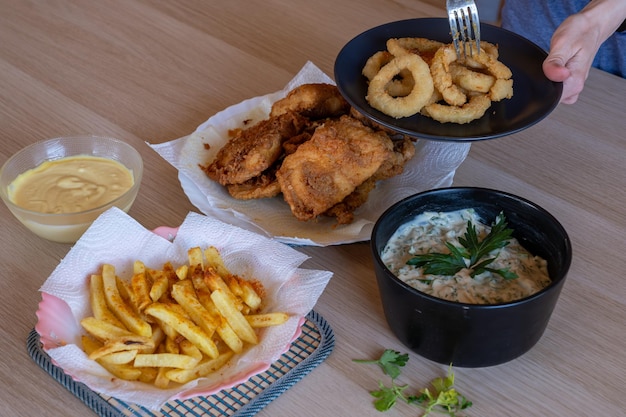 Crispy chicken fillet on wooden table served with french fries and dips and onion rings home made