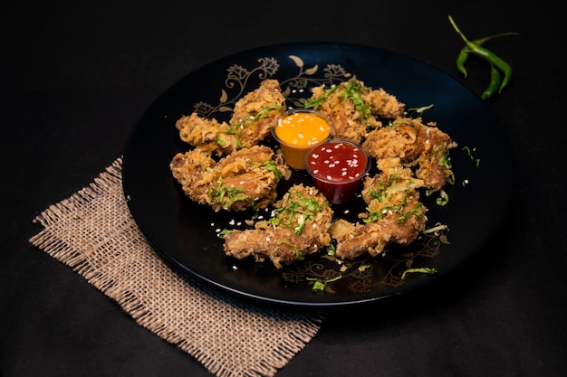 Foto ali di pollo croccanti con salsa di peperoncino e salsa di maionese servite in un piatto isolato su un tovagliolo sullo sfondo scuro vista superiore del fast food indiano