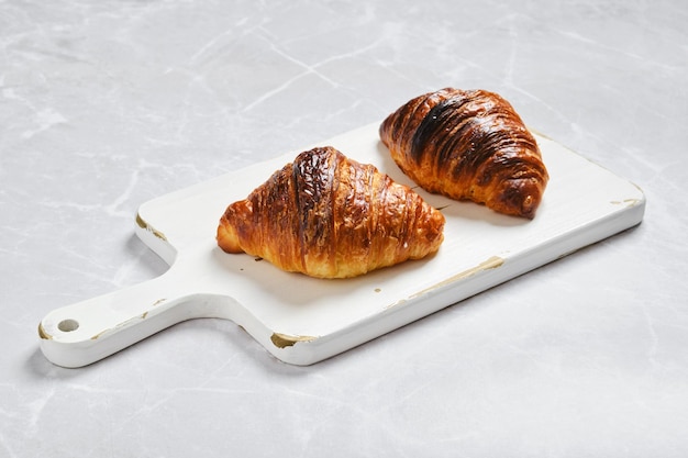 Crispy croissant on serving board on marble background