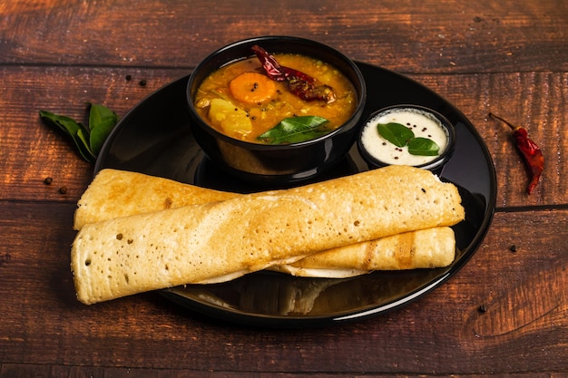 Photo crispy dosa or little millet dosa on a black plate. served with sambar and chutney. dosa.