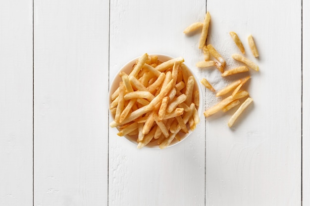 Crispy french fries in bowl on white wooden table