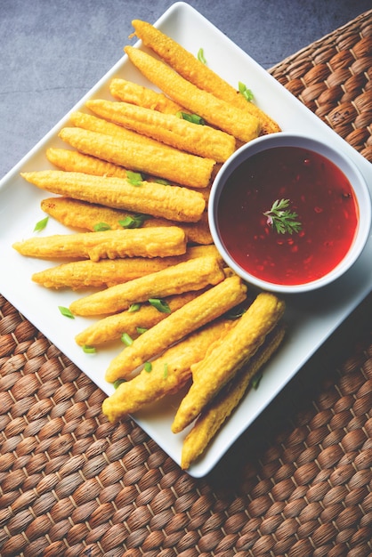 Crispy fried baby corn pakoda pakora or Baby corn fritters served with ketchup Indian food