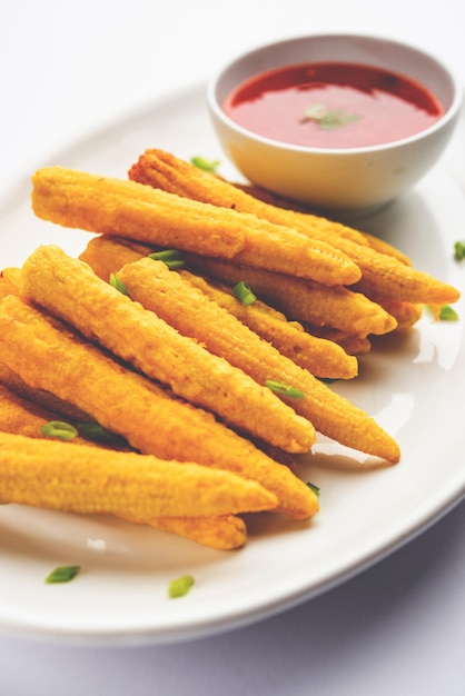 Crispy fried baby corn pakoda pakora or Baby corn fritters served with ketchup Indian food