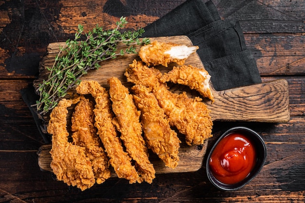 Fritto croccante strisce di pollo impanato filetto di petto di carne con ketchup su un piatto backgrund in legno vista dall'alto