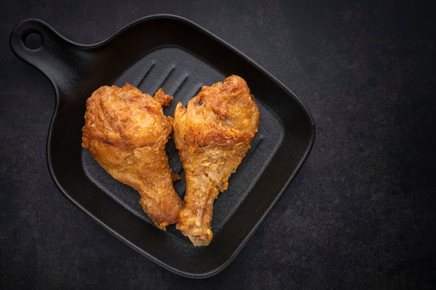 crispy fried chicken drumstick in black pan on the dark tone background, top view