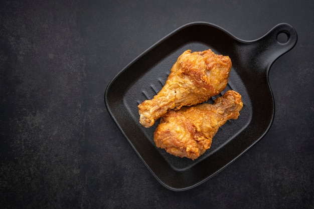 Crispy fried chicken drumstick with black pan on the dark tone background