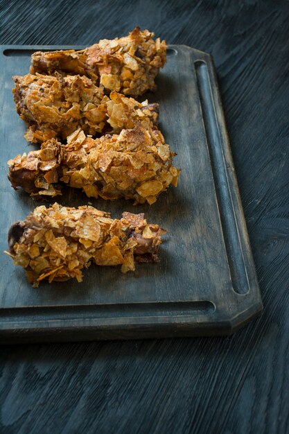 Crispy fried chicken legs breaded with chips. Fast food. Wrong food. Dark wooden table.