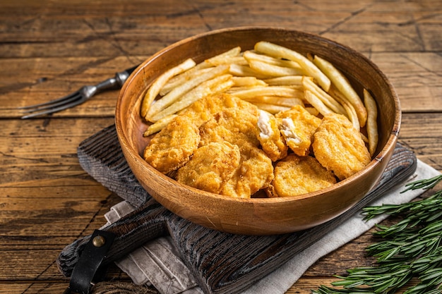 Crispy fried Chicken nuggets with French fries in wooden plate. Wooden background. Top view.