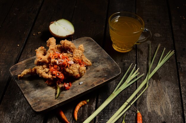 Crispy fried chicken pieces and sambal matah bali with a glass of hot orange on a wooden table