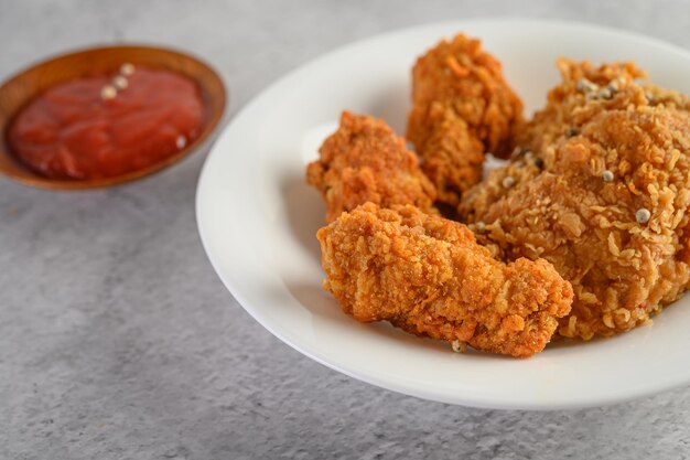 Photo crispy fried chicken on a white plate with tomato sauce