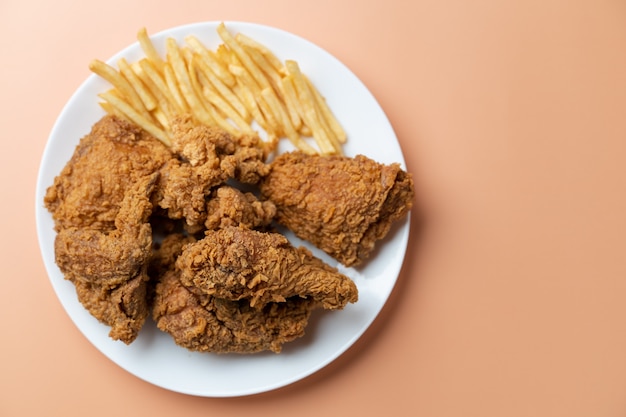Crispy fried chicken with french fries in white plate on orange background.