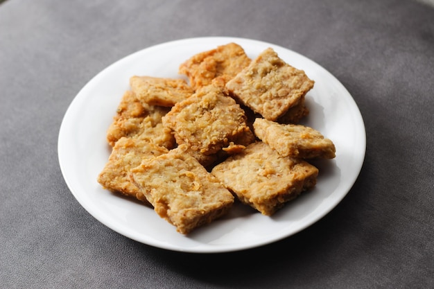 Crispy fried tempeh on a white plate with a gray background