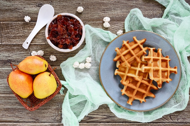 Crispy golden vanilla waffles with pear jam on a wooden background. Top view.