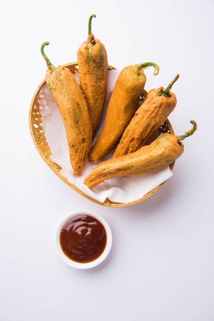 Crispy Green Chilli Pakora or Mirchi Bajji, served with tomato ketchup over moody background. Its a popular tea time snack from India especially in Monsoon. Selective focus