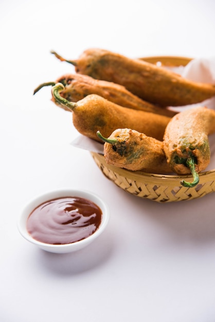 Crispy Green Chilli Pakora or Mirchi Bajji, served with tomato ketchup over moody background. Its a popular tea time snack from India especially in Monsoon. Selective focus