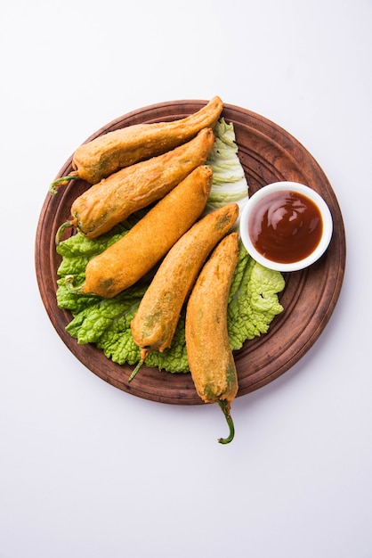 Crispy Green Chilli Pakora or Mirchi Bajji, served with tomato ketchup over moody background. Its a popular tea time snack from India especially in Monsoon. Selective focus