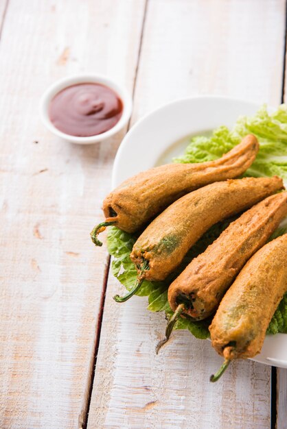 Crispy Green Chilli Pakora or Mirchi Bajji, served with tomato ketchup over moody background. Its a popular tea time snack from India especially in Monsoon. Selective focus