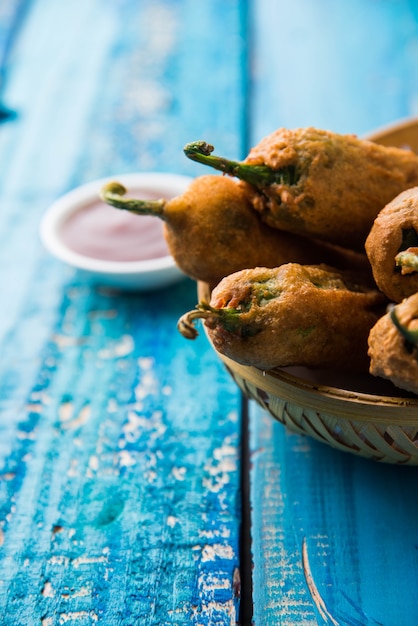Crispy Green Chilli Pakora or Mirchi Bajji, served with tomato ketchup over moody background. Its a popular tea time snack from India especially in Monsoon. Selective focus