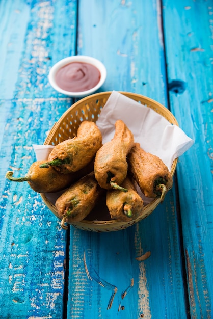 Crispy Green Chilli Pakora or Mirchi Bajji, served with tomato ketchup over moody background. Its a popular tea time snack from India especially in Monsoon. Selective focus