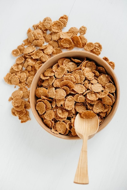 Crispy healthy dry cereal flakes in a wooden bowl with wooden spoon on white background