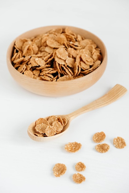 Crispy healthy dry cereal flakes in a wooden bowl with wooden spoon on white background