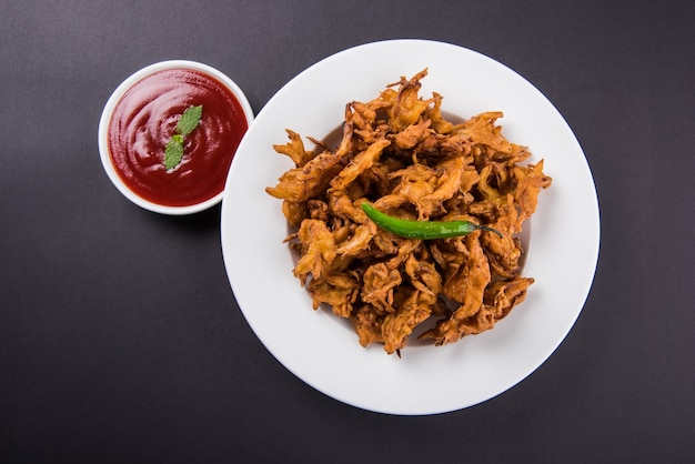 Crispy Kanda bhaji or Bhajji or Pyaj Pakode or fried onion pakora, delicious street food, favourite indian snack in monsoon served with tomato ketchup and Hot Tea