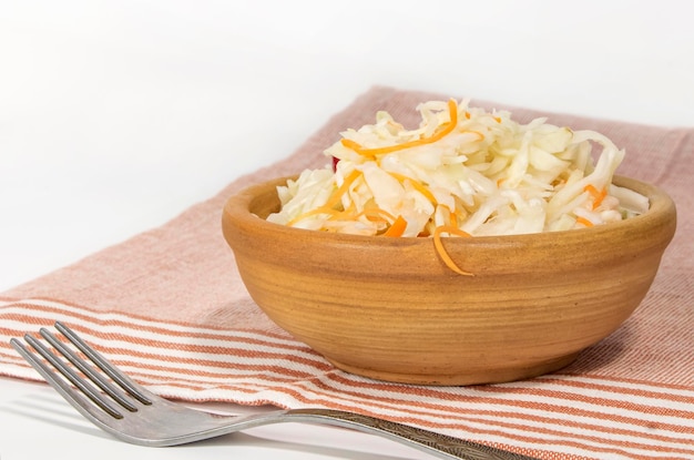 Crispy pickled cabbage in a clay bowl with a fork on the table