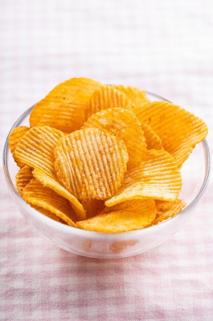 Crispy potato chips in bowl on pink checkered tablecloth