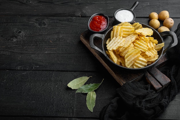 Patatine croccanti. fette di patate, arrostite con set di sale marino, su fondo di legno nero, con spazio di copia per il testo