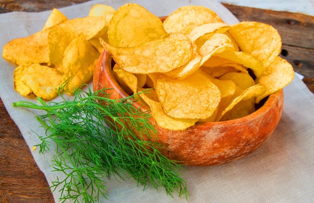 Crispy potato chips with dill in a wooden bowl on linen napkin