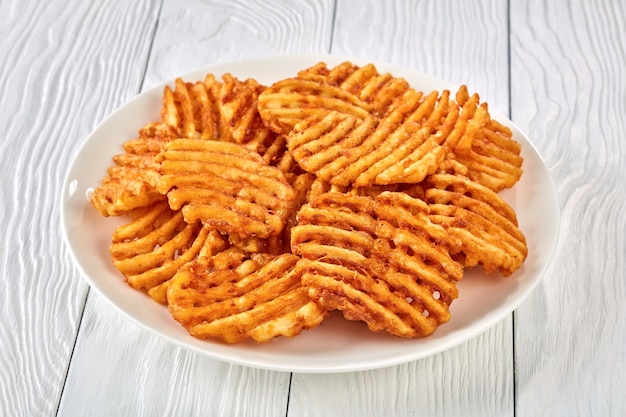 Cialde di patate croccanti patatine fritte, ondulate, crinkle cut, criss cross fries su una piastra bianca su una tavola di legno, vista da sopra, close-up