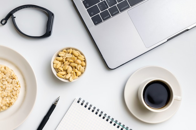 Crispy rijstrondes met pinda's, kopje koffie bij de laptop, fitness-tracker en notebook.