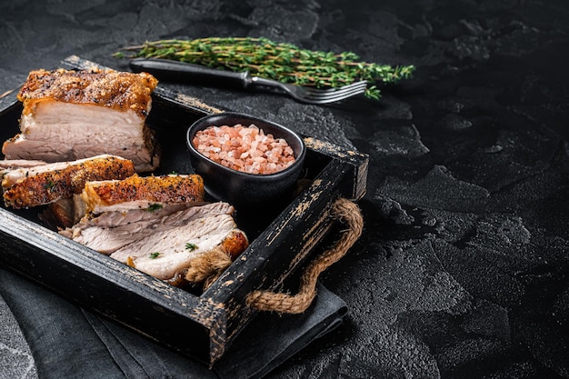 Crispy Roast Pork Belly Sliced roasted meat with crust in a tray with spices Black background Top view Copy space