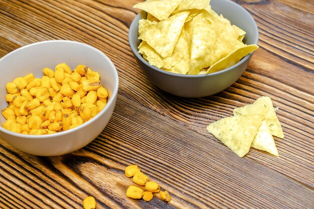 Crispy salt snacks, chips, nut, corn in bowl on wooden background close up. Unhealthy junk food, bar drink party concept, close up