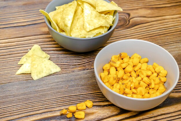 Crispy salt snacks chips nut corn in bowl on wooden background close up Unhealthy junk food bar drink party concept