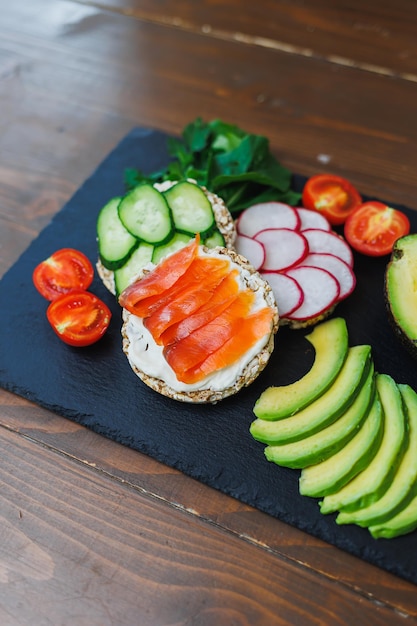 Crispy sandwich with red fish Snacks Bread and fitness food Rice bread and avocado parsley cherry tomatoes on a dark background