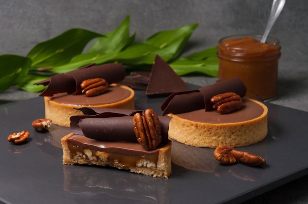 Crispy shortbread tartlet stuffed with fried pecans and creamy caramel decorated with ganache on milk chocolate